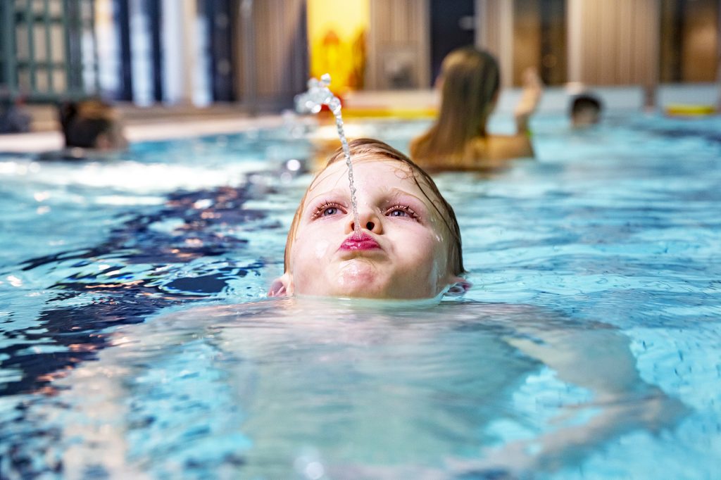 Pojke simmar och blåser en vattenstråle ur munnen.
